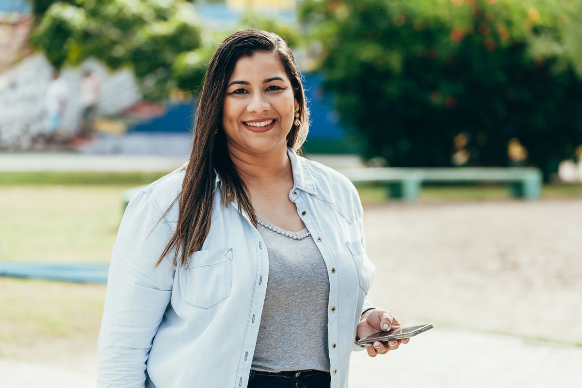 A woman standing confidently in a park, holding a cell phone.