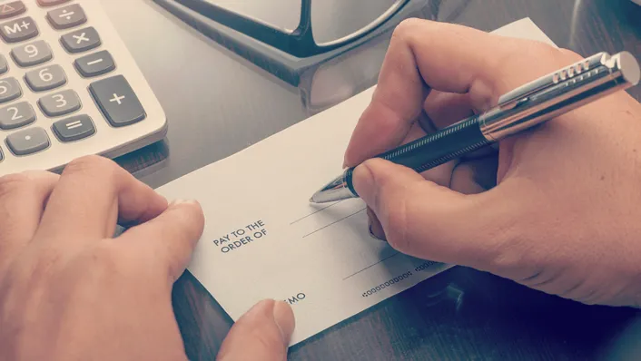 hands writing check at desk with pen