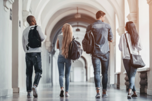 A group of students walking down a corridor in side of building with high archways