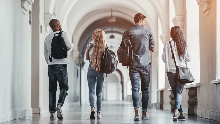 A group of students walking down a corridor in side of building with high archways