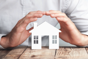 Hands hovering over a miniature house on a table.