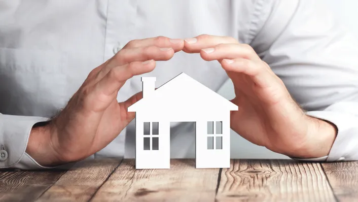 Hands hovering over a miniature house on a table.