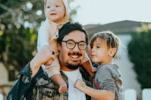 Father with glasses, holding young children, in arms and on shoulders