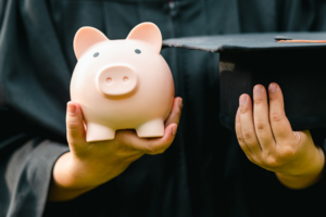 student holding piggy bank and graduation cap