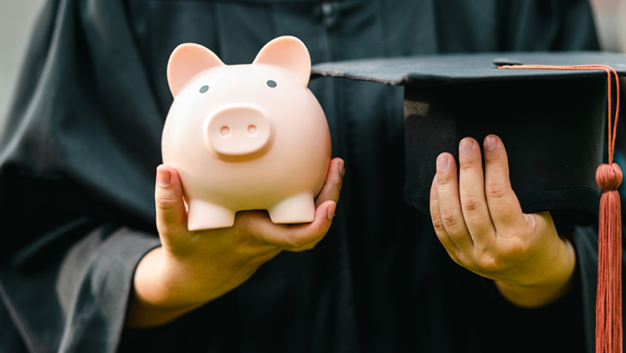 student holding piggy bank and graduation cap