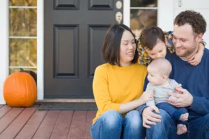 A young family sitting in front of a house. The children are showing affection to one another.