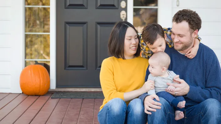 A young family sitting in front of a house. The children are showing affection to one another.