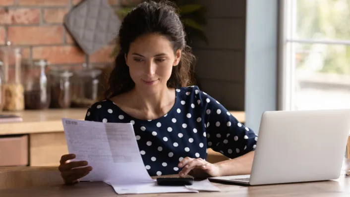 Young lady reading paper by computer.