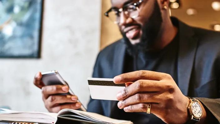 Man with glasses and watch holding credit card, entering information on phone