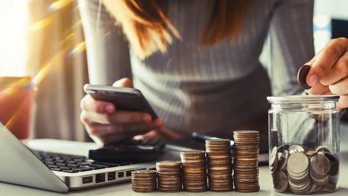 A person standing over a laptop while counting a coin jar