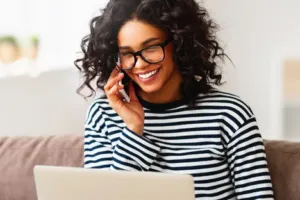 women with curly hair and glasses on the phone and laptop