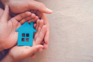 Two sets of hands holding onto a small blue house toy.