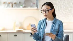 A woman enters her credit card information into a cellphone.