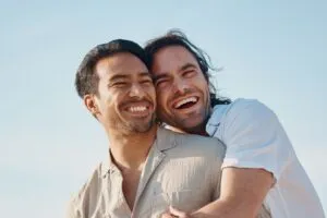 Two men in linen shirts smiling, embracing, laughing outside