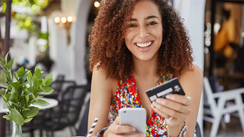 A smiling woman enters credit card information into her phone.