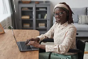 Young African American Woman in Wheelchair Using Laptop at Desk