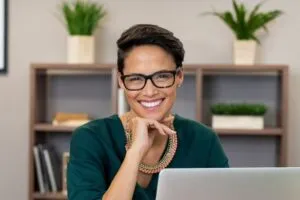 Woman with glasses in home office smiling at camera