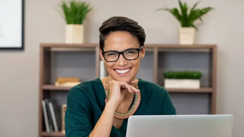 Woman with glasses in home office smiling at camera