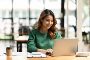 woman on laptop in office with coffee, laptop, and notepad