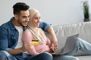 Young couple staring at a computer screen, smiling with a credit card in hand.