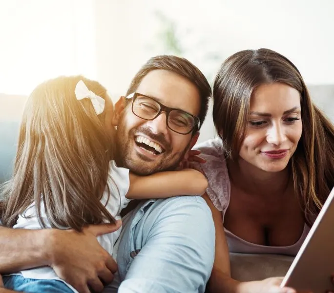 young family embracing on couch with sunglow through window