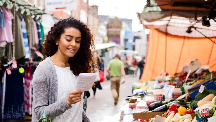 woman shopping in open stall market looking at shopping list