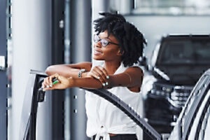 Image of woman with glasses holding car keys, arms crossed over open car door