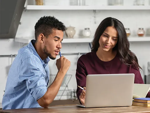 Two individuals looking at a laptop together taking notes.