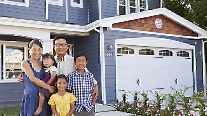 Asian family standing in front of blue residential house smiling at camera