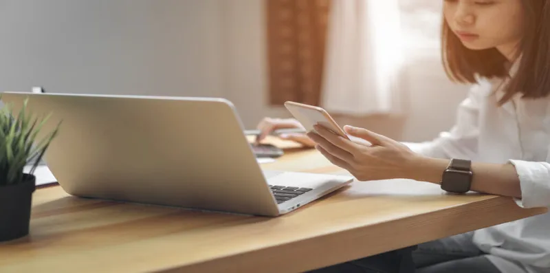 A woman calculates bills using her phone and a calculator.