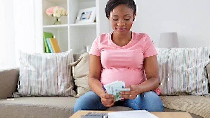 Pregnant Woman in t-shirt on couch, holding checks, bills, receipts