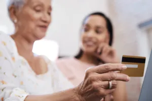 Elderly woman with daughter, holding credit card while using computer