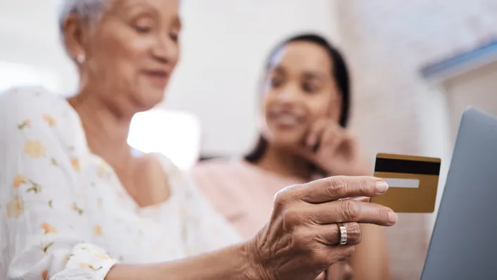 Elderly woman with daughter, holding credit card while using computer