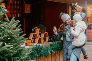 Woman holiday shopping with child in front of store window with christmas tree