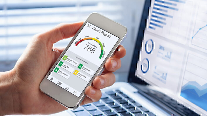 hand holding mobile phone showing credit scores in front of a laptop