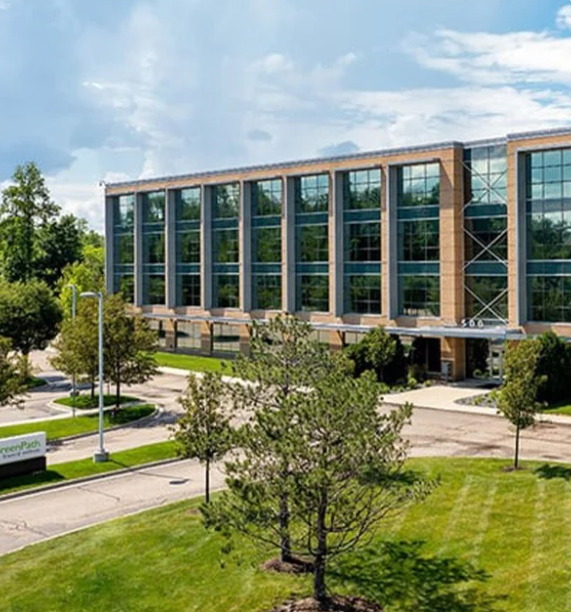 Brick office building with rows of windows, facing drive and lawn with trees