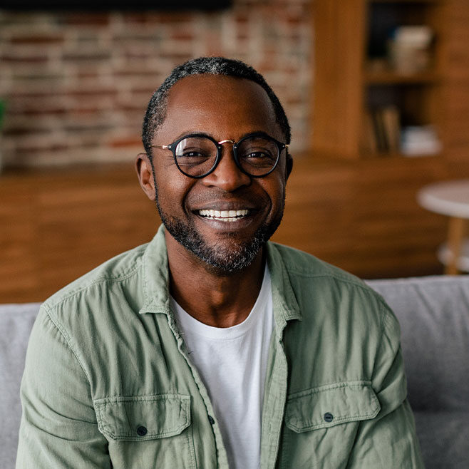 A man smiles while sitting on a comfortable couch.