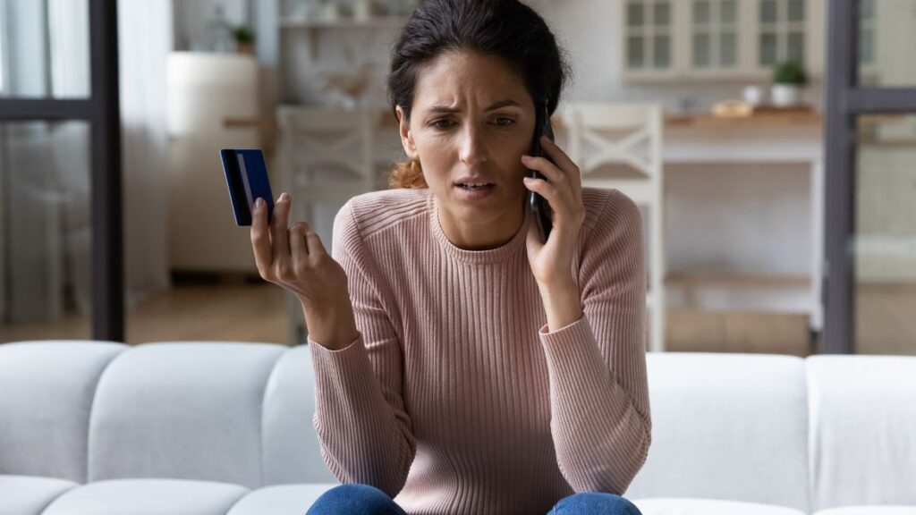 A frustrated person talking on the phone and holding up their credit card