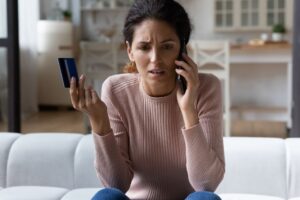 A frustrated person talking on the phone and holding up their credit card