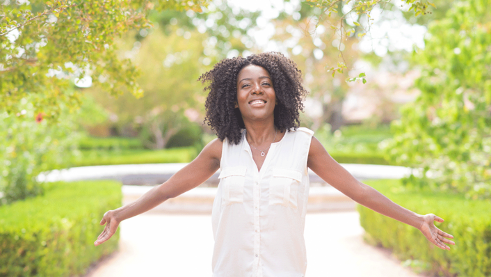 african american woman walking outside with her arms open smiling at camera