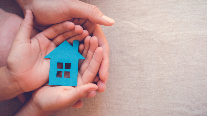 parent and child's hands holding a blue cardboard house.