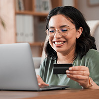 A younger person holding out their debit card inf front of a open laptop