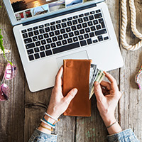 A person pulling out money and cards out in front of a laptop