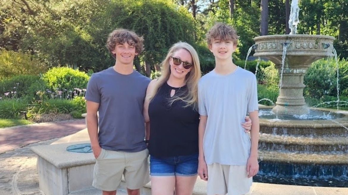 A mom with two boys posing infront of a water fountain.