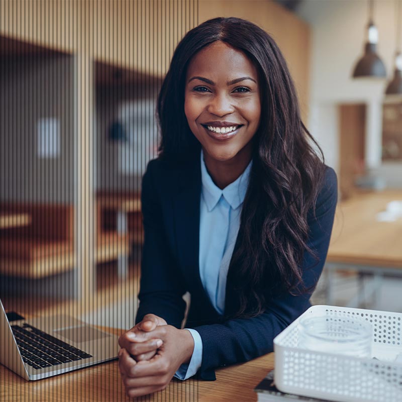 Black woman in blue blue and navy blue jacket sitting at an office desk.