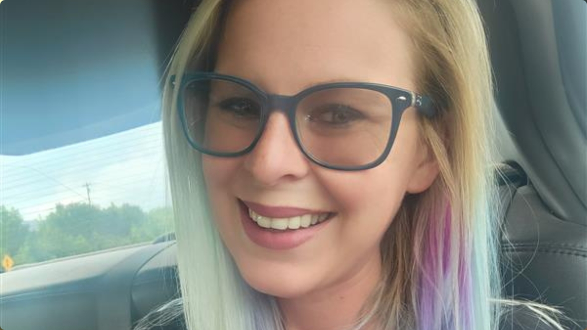 a blonde woman with purple streaks in her hair, wearing big glasses, smiling at the camera