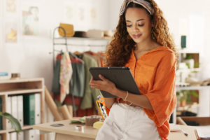 black woman with long curly hair wearing an orange blouse working on her tablet