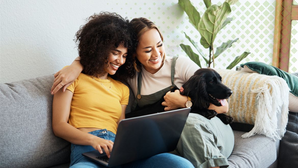 Two women sitting on the couch with their pet dog